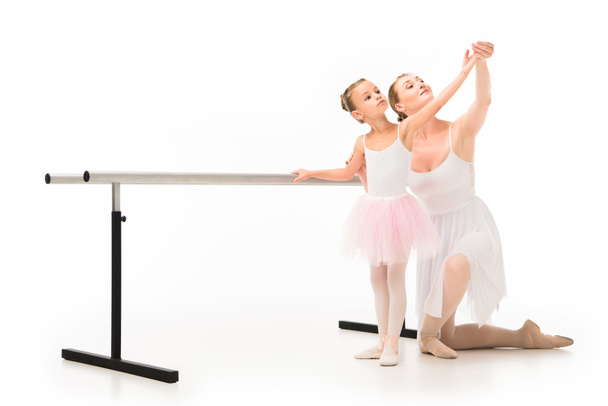 happy female teacher in tutu helping little ballerina exercising at ballet barre stand isolated on white background  - Photo, Image