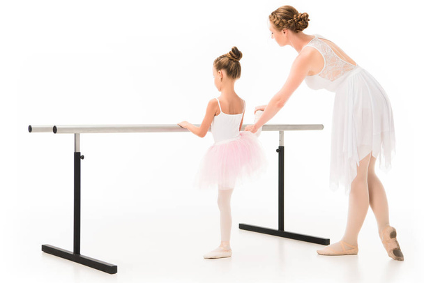 Rückansicht einer erwachsenen Lehrerin im Tutu, die einer kleinen Ballerina beim Ballettunterricht hilft, steht isoliert auf weißem Hintergrund  - Foto, Bild