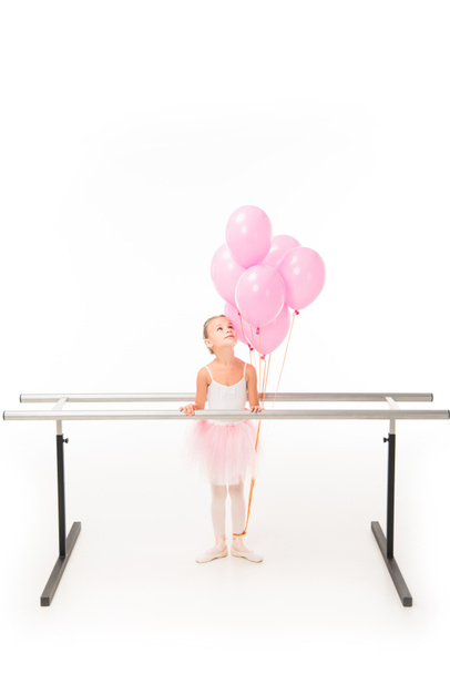 pequena bailarina em tutu em pé no ballet barre stand e olhando para balões rosa isolado no fundo branco
  - Foto, Imagem