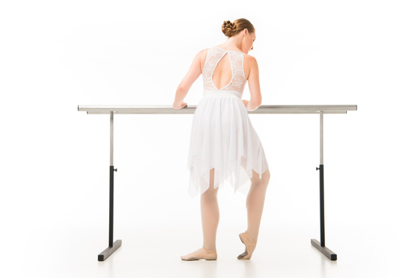 rear view of adult ballerina in tutu exercising at ballet barre stand isolated on white background  - Fotó, kép