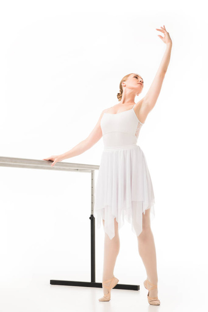 elegant ballerina in tutu and pointe shoes practicing at ballet barre stand isolated on white background  - Photo, Image