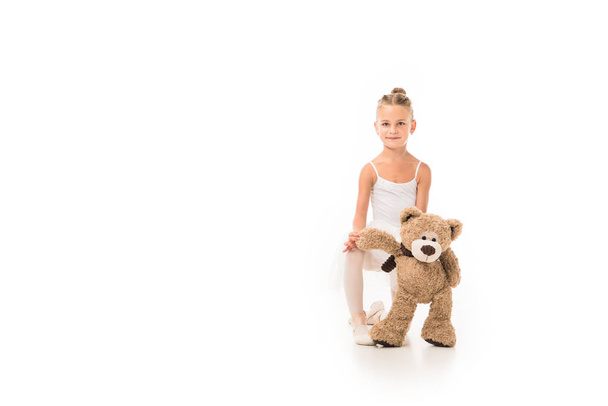 adorable little ballerina in tutu sitting with teddy bear isolated on white background  - Фото, изображение