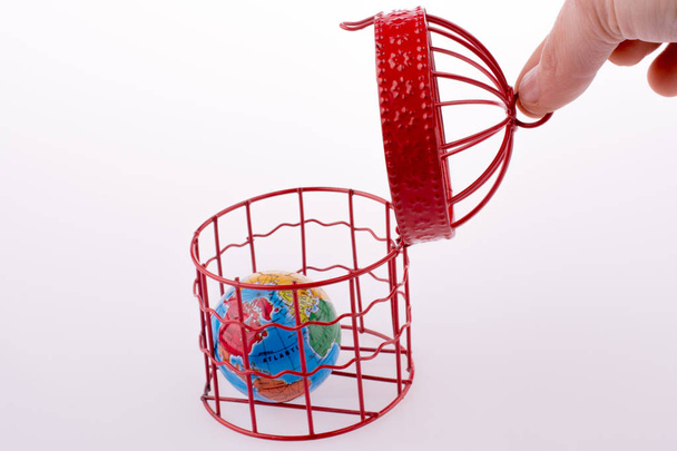 Kleiner Globus gefangen in einem roten Vogelkäfig - Foto, Bild