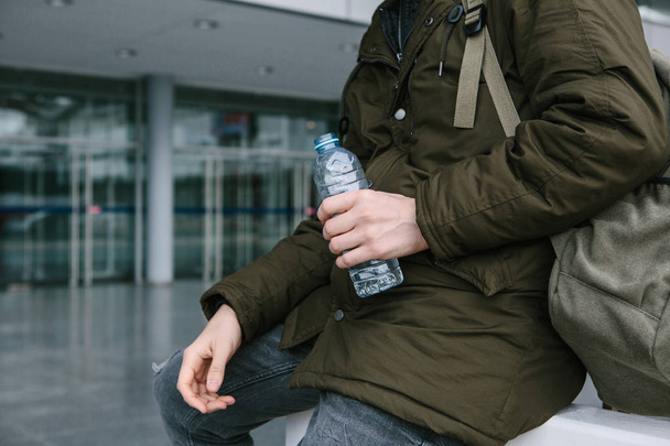 Ο ταξιδιώτης κρατά ένα μπουκάλι νερό στο χέρι του. - Φωτογραφία, εικόνα