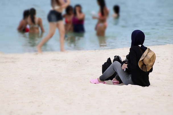 Muzułmanin dziewczyna podróżnik na hidżab siedzi na piaszczystej plaży - Zdjęcie, obraz