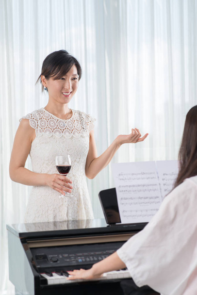 young asian woman with red wine glass listening to music of friend playing piano  - Photo, Image