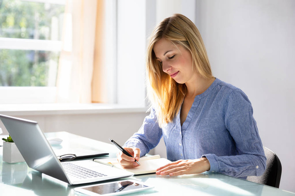 Businesswoman Writing Schedule In Diary With Electronic Devices On Desk - Foto, Imagen