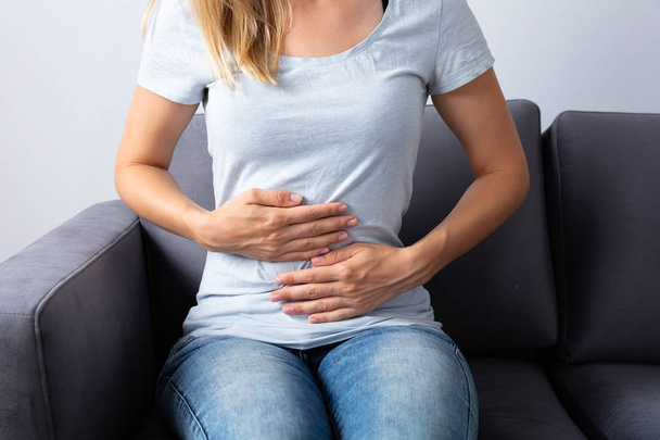 Woman Sitting On Sofa Suffering From Stomach Pain - Foto, immagini