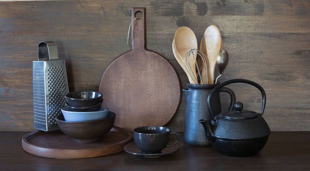 Crockery, clayware, dark utensils and other different stuff on wooden tabletop. Kitchen still life for cooking as background for design. Copy space. - Photo, Image