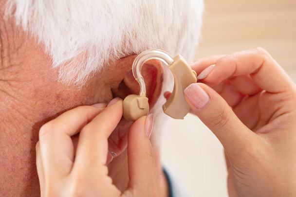 Female Doctor's Hand Inserting Hearing Aid In Senior Male Patient's Ear - Фото, изображение