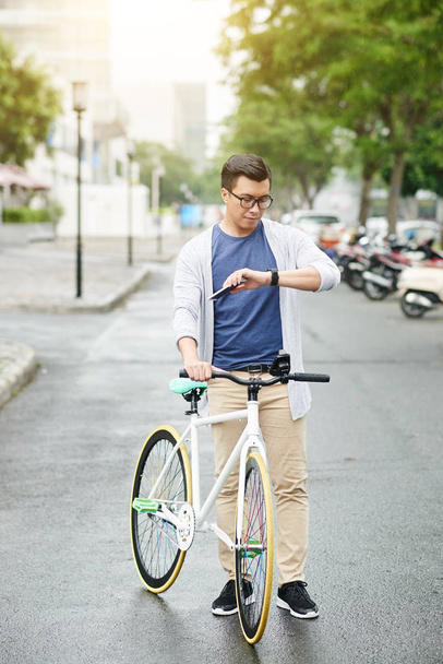 アジア系の若い男と自転車の彼のスマートウォッチの情報をチェック - 写真・画像