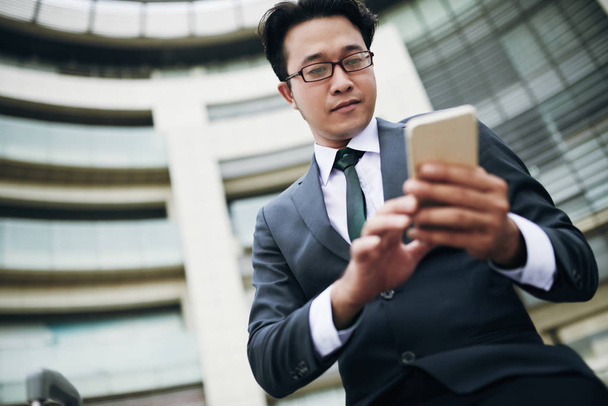 Low angle view of Asian businessman text messaging on smartphone  - Photo, Image