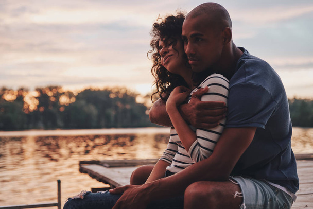 romantic couple in love embracing and sitting on pier at lake  - Φωτογραφία, εικόνα