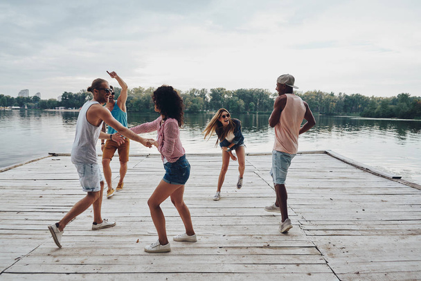 full length of playful friends enjoying beach party on wooden pier at lake  - Valokuva, kuva
