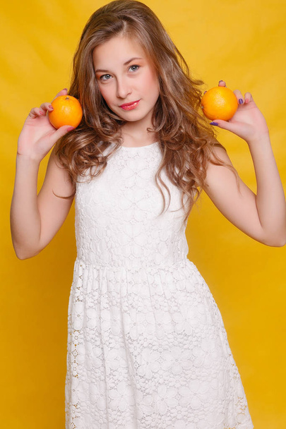 Young beautiful funny fashion model with orange slice on orange background. with makeup and hairstyle. holding lemon with nice smile. - Foto, afbeelding