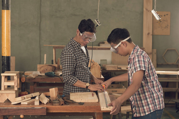 fils et père menuisiers travaillant avec du bois en atelier, mesurant des planches de bois
 - Photo, image