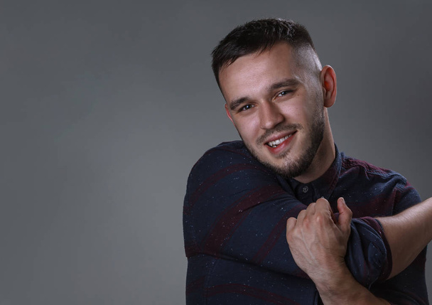 Friendly young man smiling in to the camera. Half side portrait handsome in checkered and cross hands. Copy space grey background - Fotografie, Obrázek