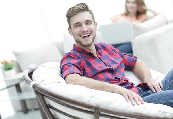 glücklicher junger Mann sitzt in einem großen Stuhl auf verschwommenem Hintergrund - Foto, Bild