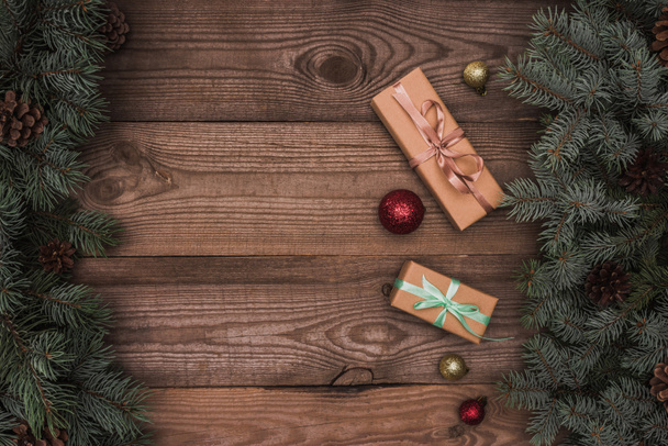top view of christmas presents, shiny baubles and coniferous branches with pine cones on wooden background - Foto, Imagen