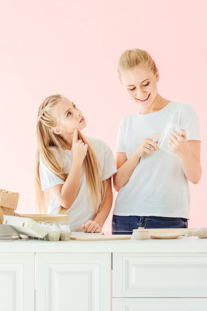 beautiful mother and daughter in white t-shirts cooking together isolated on pink - Fotografie, Obrázek