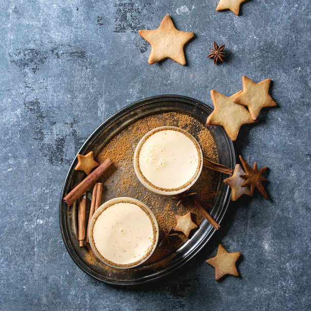 Eggnog Christmas milk cocktail with cinnamon, served in two glasses on vintage tray with shortbread star shape sugar cookies different size over blue texture background. Top view with space. Square image - Zdjęcie, obraz