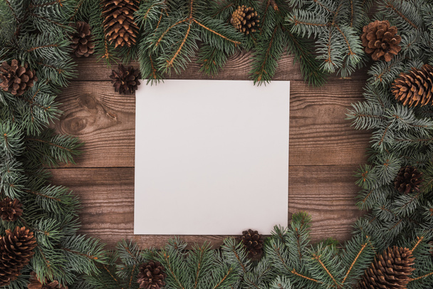 top view of blank card and coniferous branches with pine cones on wooden background - Foto, Imagen