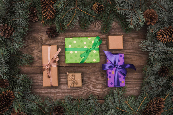 верхний вид завернутых рождественских подарков и хвойных ветвей с сосновыми шишками на деревянном фоне
 - Фото, изображение