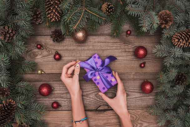 cropped shot of person opening christmas present on wooden surface with festive decorations - Photo, Image