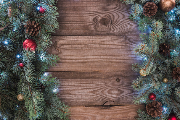 το Top view κωνοφόρων κλαδιά με λαμπερά στολίδια, κουκουνάρια και φωτιζόμενο γιρλάντα Χριστουγέννων φόντο - Φωτογραφία, εικόνα