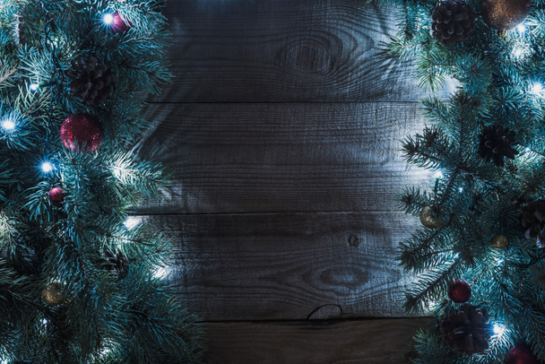 top view of beautiful christmas tree branches with baubles, pine cones and illuminated garland on wooden background  - Photo, Image