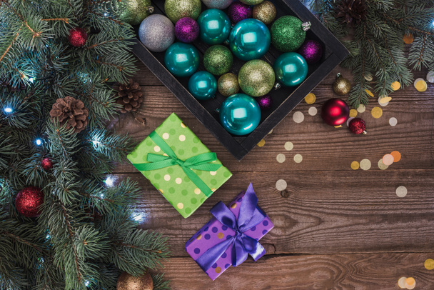 top view of beautiful colorful shiny baubles, gift boxes and fir twigs on wooden background  - Foto, Imagen