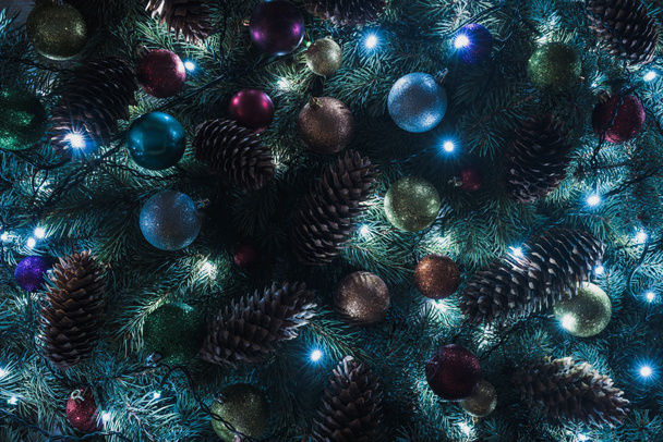Nahaufnahme des schönen Weihnachtsbaums mit Tannenzapfen, bunten Kugeln und beleuchteter Girlande  - Foto, Bild