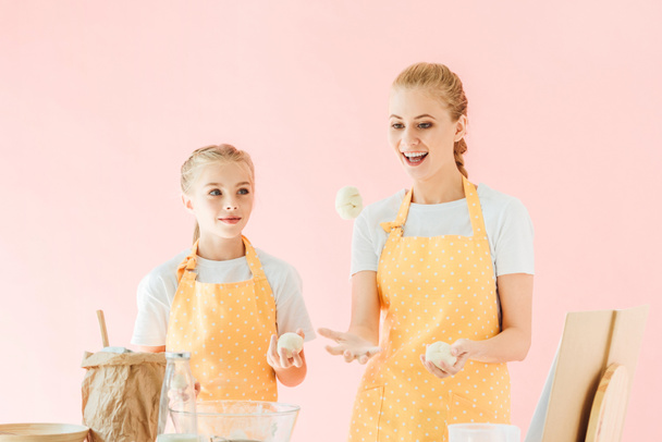 hymyilevä äiti ja tytär jongleerausta taikinan kappaletta, kun ruoanlaitto eristetty vaaleanpunainen
 - Valokuva, kuva