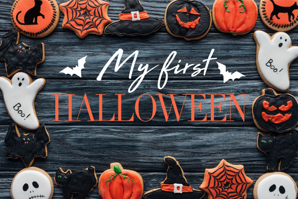 frame made of spooky halloween homemade cookies on black wooden background with bats "my first halloween" lettering  - Photo, Image