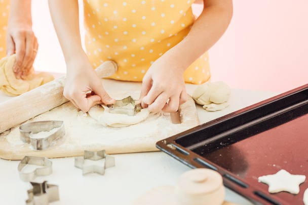 bijgesneden shot van het kleine meisje snijden deeg in verschillende vormen voor koekjes met moeder - Foto, afbeelding