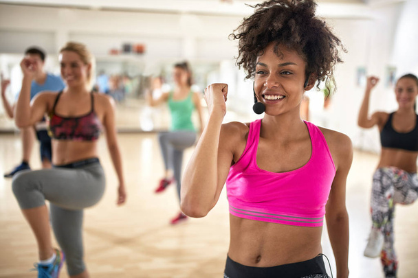 Pretty female instructor with headset in fitness class exercise with group  - Foto, afbeelding