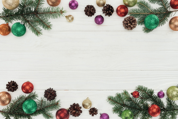 top view of colorful shiny christmas balls, fir twigs and pine cones on white wooden background - Photo, Image