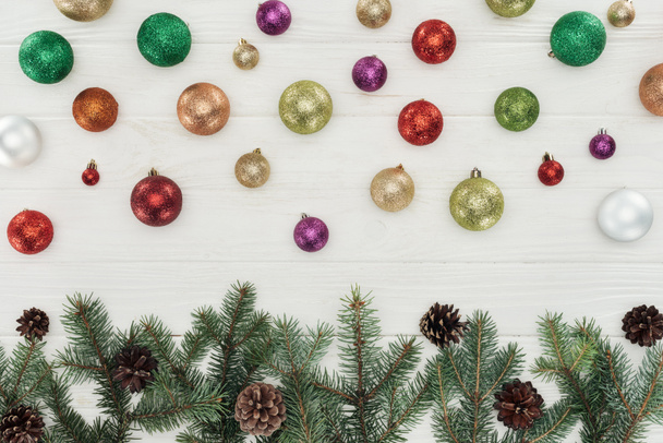 beautiful shiny colorful christmas balls and fir twigs with pine cones on white wooden background  - Fotografie, Obrázek