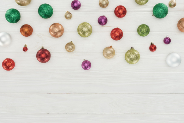 Blick von oben auf schöne glänzende bunte Weihnachtskugeln auf weißem Holzhintergrund  - Foto, Bild