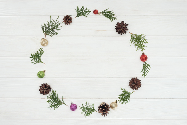 top view of evergreen coniferous twigs, pine cones and baubles on wooden background  - Foto, imagen