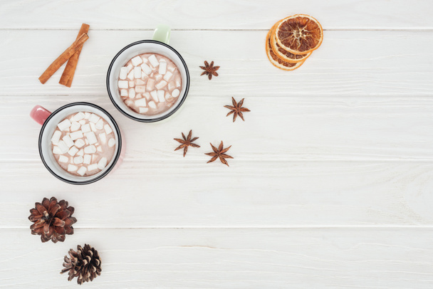 flache Lage mit Tassen mit heißer Schokolade und Marshmallows, Zimtstangen und Tannenzapfen auf Holztisch - Foto, Bild