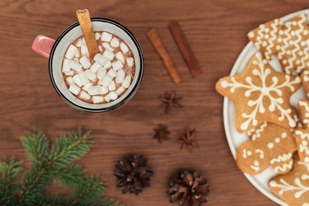 Draufsicht auf Tasse mit heißer Schokolade und Marshmallows, Zimtstangen und Lebkuchen  - Foto, Bild