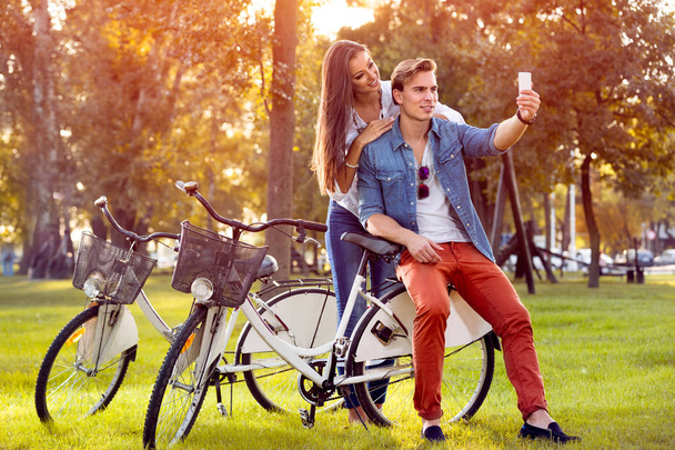 smiling couple with bicycles and smartphone in autumn park  - Фото, зображення