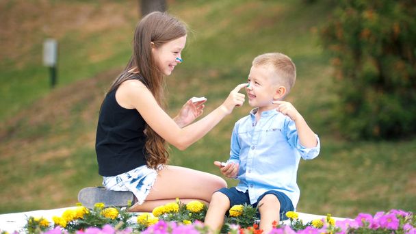 Little blonde girl and her younger friend are playing with paint in the park - 写真・画像