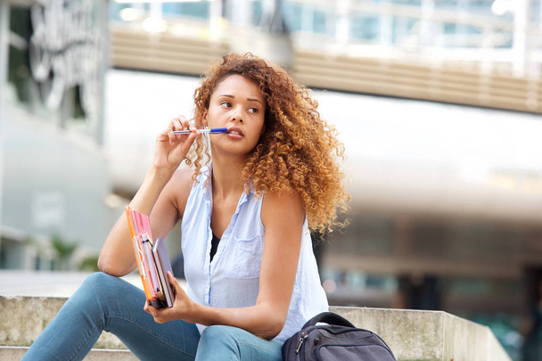 Porträt einer Studentin, die mit Buch und Stift draußen sitzt - Foto, Bild