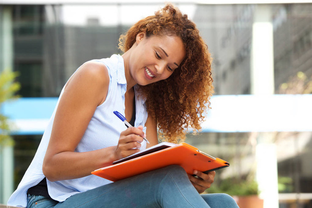 Retrato lateral de una joven sentada y escribiendo en libro con pluma
 - Foto, Imagen