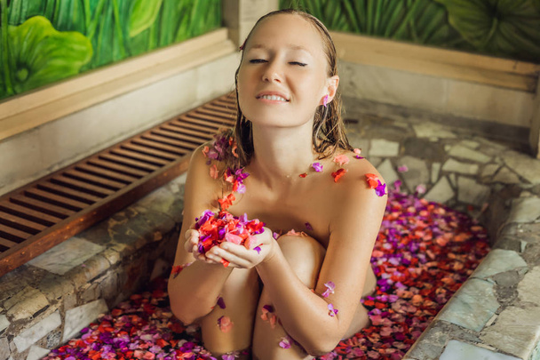 Young woman enjoying spa bath with petals of tropical flowers and aroma oil. - Fotoğraf, Görsel