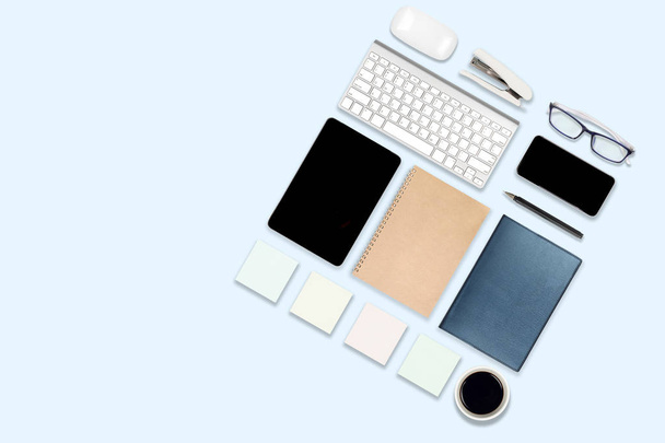 ラップトップ コンピューター、デジタル タブレット、携帯電話、アクセサリーとのオフィスのテーブルのフラット レイアウトの写真。分離された青い背景。デスクトップ オフィス モックアップ コンセプト. - 写真・画像