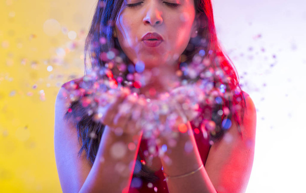 Beautiful girl on party background blowing confetti - Valokuva, kuva
