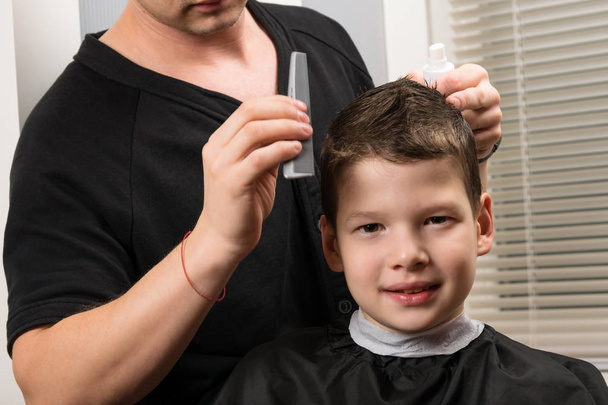 the boy is sitting in the beauty salon, he is made with hair styling - Foto, afbeelding